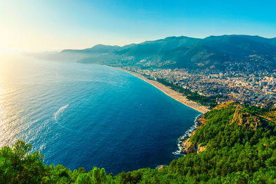 Aerial view of sea by city against clear blue sky on sunny day