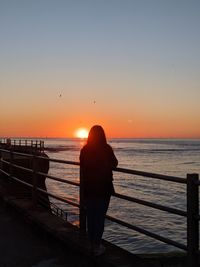 Silhouette woman looking at sea against sky during sunset