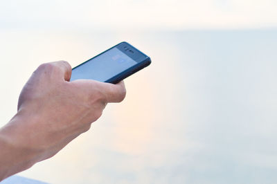 Midsection of person holding mobile phone against sky