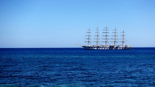 Sailboat sailing in sea against clear blue sky