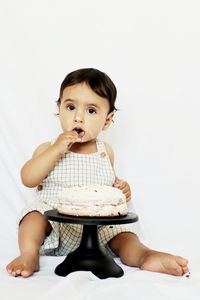 Portrait of cute baby boy eating cake sitting against white background