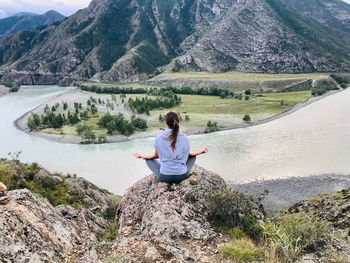 Yoga girl sitting on rock by mountains