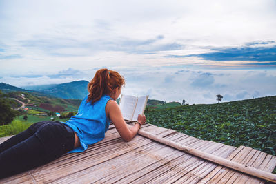 Rear view of woman sitting on mountain against sky