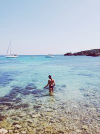 Rear view of young woman standing on shore against clear sky