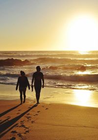 Silhouette friends walking on beach against sky during sunset