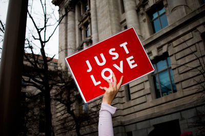 Cropped hand holding just love sign against building