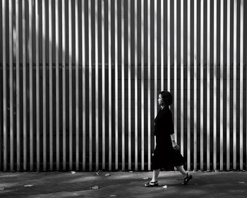 Side view of woman walking on road against wall