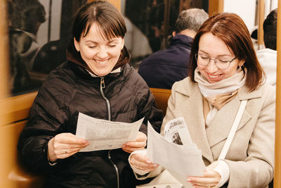 Portrait of two beautiful cheerful girls reading newspapers in a subway car.