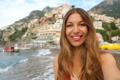 Portrait of smiling young woman standing at beach in city