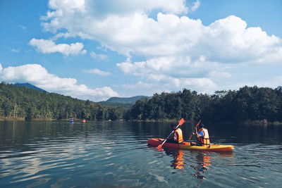 People kayaking in lake against sky