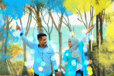 Couple holding smoke bombs while standing amidst trees