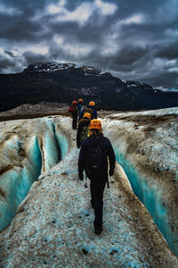 Rear view of hikers walking on rock against cloudy sky