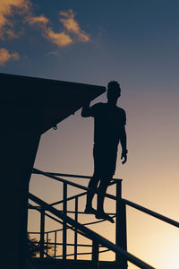 Silhouette man standing by railing against sky during sunset