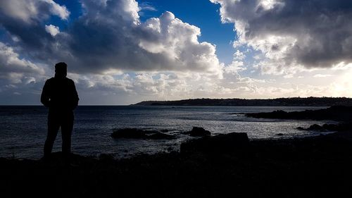 Rear view of silhouette man standing at beach against sky