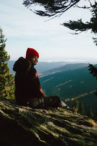 Man sitting on mountain against sky