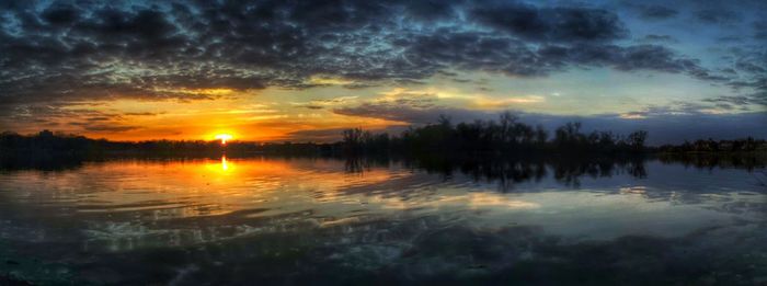 Scenic view of lake against cloudy sky at sunset