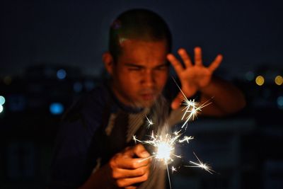 Man gesturing while holding sparkler at night