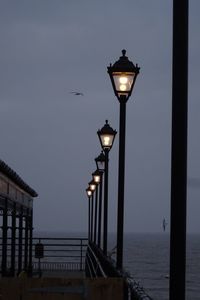 Illuminated street light by sea against sky