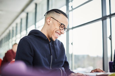 Smiling male university student studying at table in cafeteria