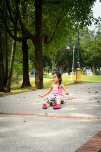 Side view of little girl sitting on the skateboard at the park