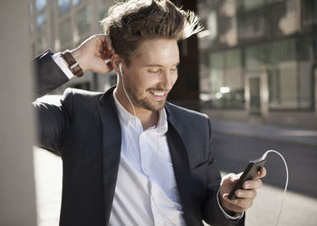 Young businessman smiling while listening music through mobile phone on street