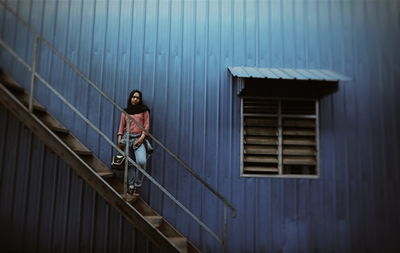 Full length of woman standing on steps against corrugated metal