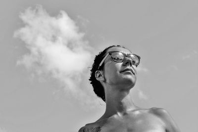 Low angle view of shirtless young woman wearing sunglasses while looking away against sky during sunny day