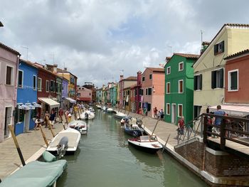 Boats moored in canal amidst buildings in city against sky