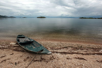 Abandoned boat moored on beach against cloudy sky