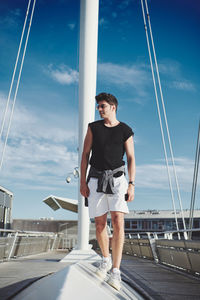 Young man standing on railing against sky