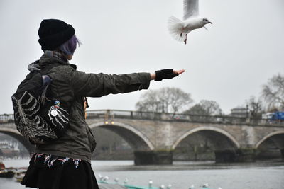 Rear view of woman standing by bridge over river against sky