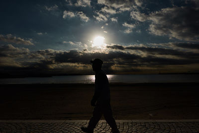 Silhouette man standing on beach against sky during sunset