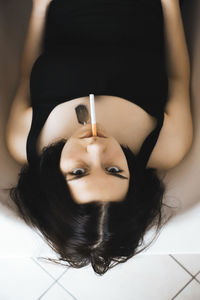 Portrait of teenager girl holding cigarette in mouth lying on floor at home