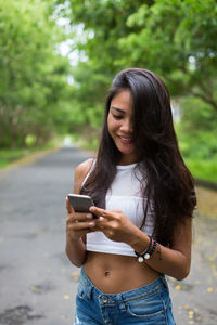 Smiling young woman using phone on road