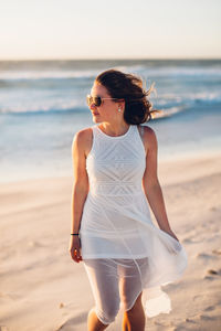 Young woman walking at beach against clear sky during sunset