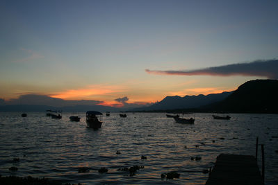 Silhouette boats in calm sea at sunset