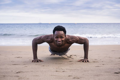 Portrait of man doing push-ups at beach