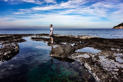 Woman standing on rock by sea against sky