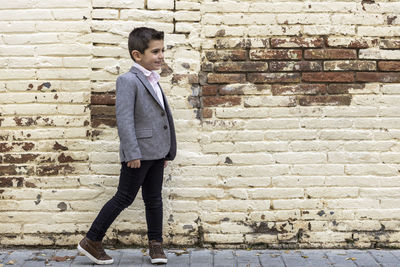 Boy looking away while walking against brick wall