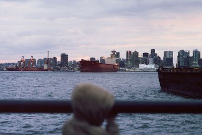 Rear view of man by sea against buildings in city