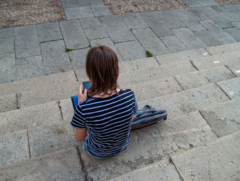 Rear view of teenage girl using mobile phone while sitting on steps