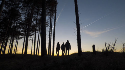 Silhouette people walking on landscape against sky during sunset