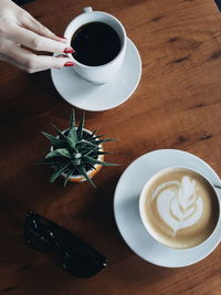 Cropped image of woman hand on coffee by potted cactus on table