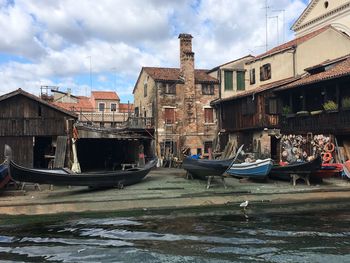 Boats moored in canal by buildings against sky