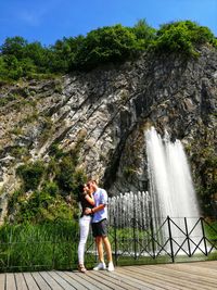 Rear view of woman standing by waterfall against trees