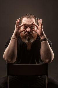 Portrait of man making funny face while sitting on chair against black background