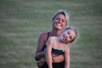 Portrait of happy mother carrying daughter while standing on field