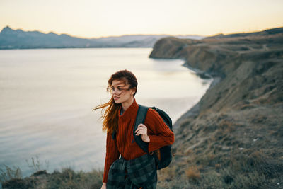 Young woman standing on shore against sky during sunset