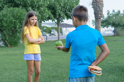 Teenage boy and girl with apple and burger in the park. choice between healthy and unhealthy food.