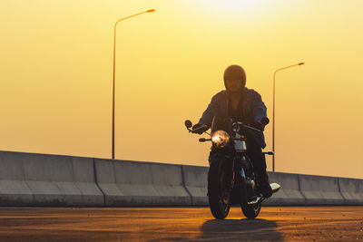 Man riding motorcycle on road against sky during sunset